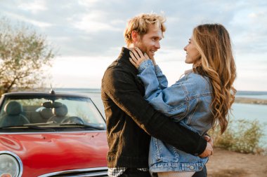 Yolculuk sırasında arabada beklerken gülümseyen ve sarılan beyaz bir çift.