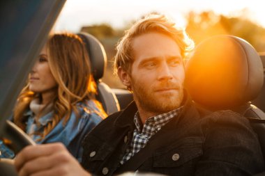 Günbatımında birlikte araba süren beyaz bir çift.