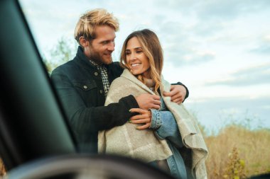 White mid couple smiling and hugging while standing by car during trip