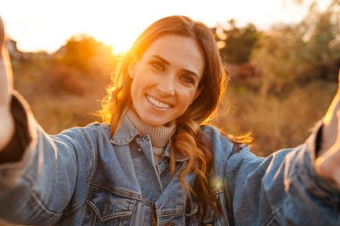 Beyaz kızıl kadın dışarıda selfie çekerken gülümsüyor.