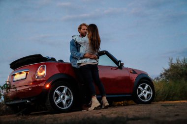 Yolculuk sırasında arabada beklerken gülümseyen ve sarılan beyaz bir çift.