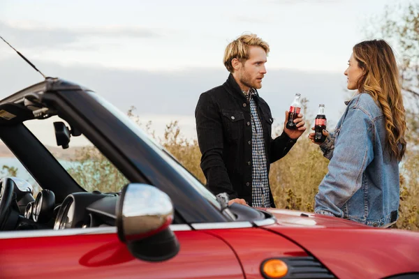 White mid couple drinking soda and talking while standing by car during trip