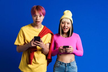 Asyalı gençler şaşkınlıklarını dile getirirken mavi duvarda izole edilmiş cep telefonları kullanıyorlar.