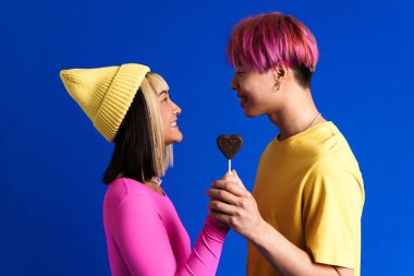 Asyalı gençler gülümserken mavi duvarda izole edilmiş kalp lolipoplarıyla poz veriyorlar.