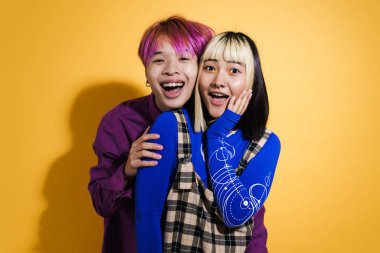 Asian couple with multicolored hair hugging and laughing together isolated over yellow wall