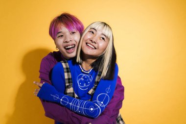 Asian couple with multicolored hair hugging and laughing together isolated over yellow wall