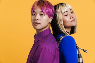 Asian couple with multicolored hair posing back to back isolated over yellow wall