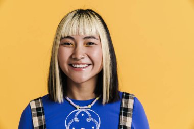 Sarı duvarın üzerinden izole edilmiş, gülümseyen ve kameraya bakan Asyalı kız.