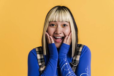 Piercingli, gülen ve sarı duvardan izole edilmiş kameraya bakan Asyalı kız.