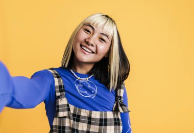 Sarı duvardan izole edilmiş selfie çekerken gülümseyen Asyalı kız.