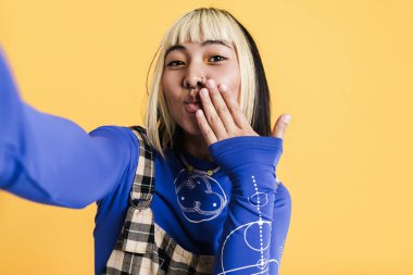 Sarı duvardan izole edilmiş selfie çekerken piercing takan Asyalı kız.