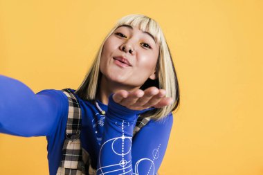 Sarı duvardan izole edilmiş selfie çekerken piercing takan Asyalı kız.