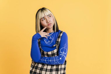 Suratı asık Asyalı bir kız, sarı duvarın üzerinden yukarı bakarken kaşlarını çatıyor.