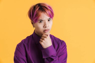 Pembe saçlı Asyalı çocuk somurtuyor ve sarı duvardan izole edilmiş kameraya bakıyor.