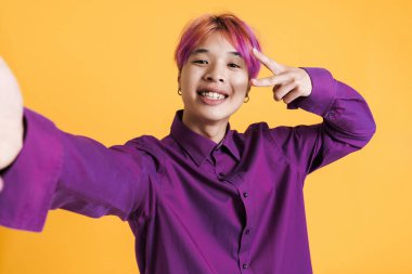 Asyalı çocuk sarı duvarda izole edilmiş selfie çekerken barış jesti yapıyor.