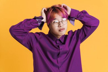 Gözlüklü Asyalı üzgün çocuk sarı duvarda tek başına başını tutarken kaşlarını çatıyor.