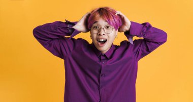 Asyalı bir çocuk sarı duvarın üzerinde şaşırdığını belirtirken başını tutuyor.