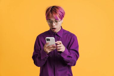 Gözlüklü Asyalı çocuk şaşırdı ve sarı duvarda izole edilmiş bir cep telefonu kullandı.