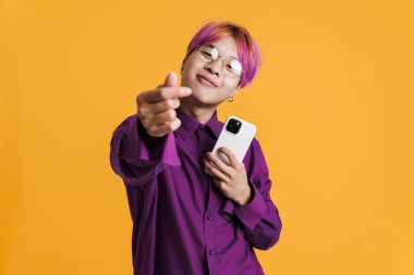 Gözlüklü Asyalı çocuk parmaklarını ovuyor ve sarı duvarda izole edilmiş cep telefonu kullanıyor.