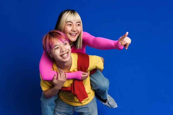 Asiático Adolescentes Apontando Dedo Afastado Enquanto Piggybacking Isolado Sobre Azul — Fotografia de Stock