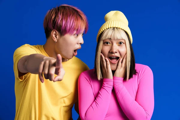 Asyalı gençler kamerayı işaret ederken mavi duvarın üzerinde izole edilmiş şaşkınlıklarını ifade ediyorlar.