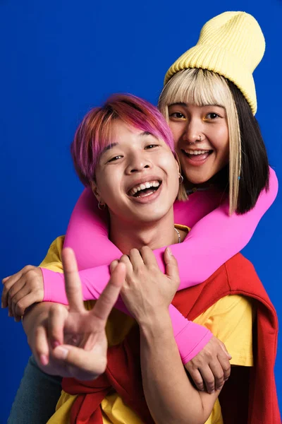 Çok renkli saçlı Asyalı çift mavi duvarın üzerinde izole bir işaret gösterirken sarılıyorlar.