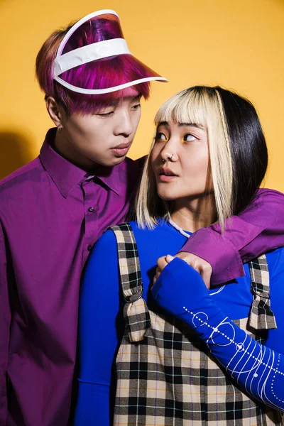 Sarılan Asyalı çift, sarı duvarın üzerinden birbirlerine bakıyorlar.