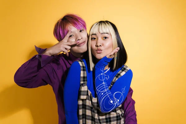 Asian couple with multicolored hair laughing and gesturing together isolated over yellow wall