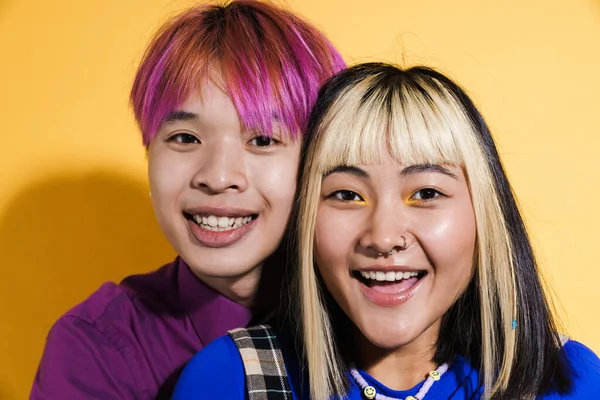 Sarılıp birlikte gülen Asyalı çift sarı duvarın üzerinde izole edilmiş.