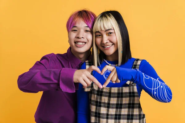 Asyalı çift gülümserken birlikte kalp hareketi gösteriyorlar. Sarı duvarın üzerinde izole edilmiş.