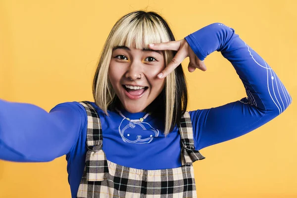 Sarı duvardan izole edilmiş selfie çekerken piercing takan Asyalı kız.