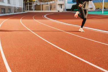 Genç beyaz sporcu dışarıda stadyumda çalışırken koşuyor.