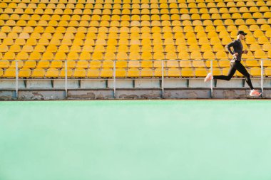 Genç beyaz sporcu dışarıda stadyumda çalışırken koşuyor.