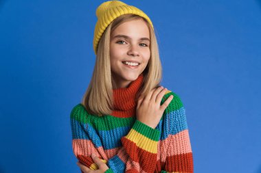Şapkalı beyaz kız gülümsüyor ve mavi arka planda izole edilmiş kameraya bakıyor.
