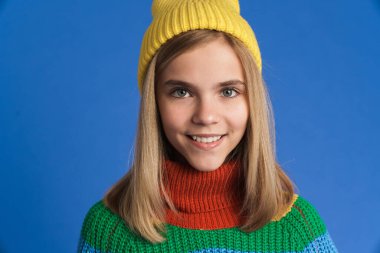 Şapkalı beyaz kız gülümsüyor ve mavi arka planda izole edilmiş kameraya bakıyor.