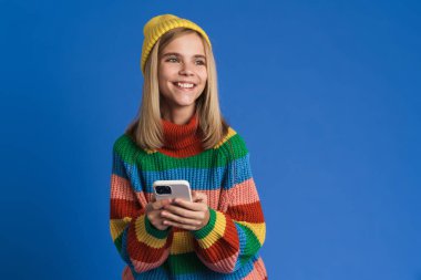 Şapka takan, gülümseyen ve mavi arka planda cep telefonu kullanan beyaz kız.