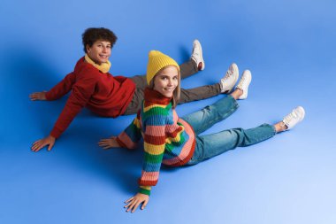 Beyaz kız ve oğlan gülümseyip kameraya bakarken mavi arka planda izole bir şekilde oturuyorlar.