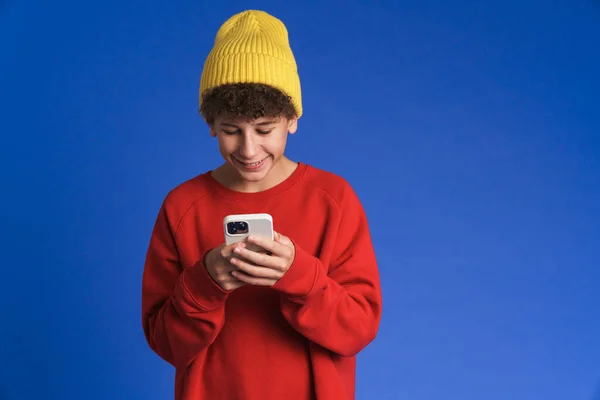 White Boy Wearing Hat Smiling Using Mobile Phone Isolated Blue — 图库照片