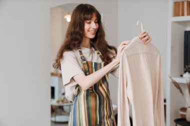 Evde ev işi yaparken önlüklü beyaz kadın gülümsüyor.