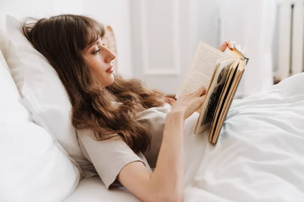 White Young Woman Reading Book While Lying Bed Home — Stok fotoğraf