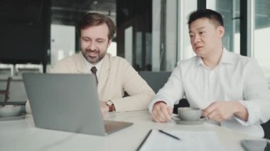 Confident multinational colleagues talking about project and watching something on laptop in the office