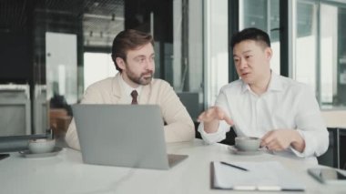 Concentrated multinational colleagues talking about project and looking at laptop in the office