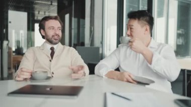 Positive multinational colleagues talking about project and drinking coffee in the office