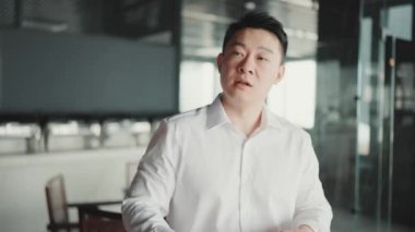 Pensive Asian brunet businessman talking something while standing in the office