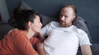 Positive couple talking while lying on the bed at home