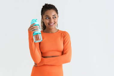 Beyaz arka planda izole edilmiş su şişesiyle poz verirken gülümseyen siyah genç sporcu kadın.