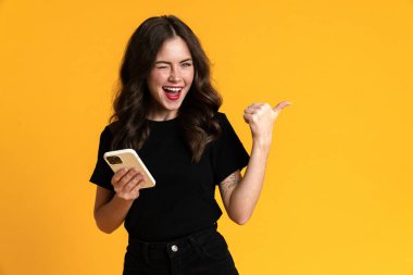 Sarı arka planda izole edilmiş cep telefonu kullanan beyaz genç bir kadın.