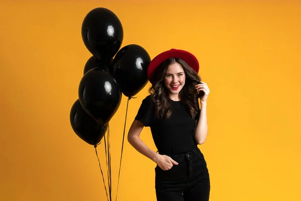 Kırmızı Şapkalı Beyaz Kadın Sarı Arka Planda Siyah Balonlarla Poz — Stok fotoğraf