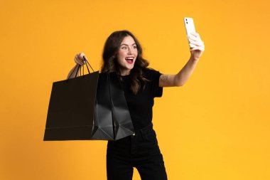 White excited woman taking selfie with shopping bags isolated over yellow background