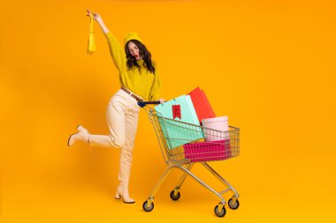 White woman making fun while posing with shopping cart isolated over yellow background